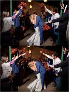 blonde bride in white gown and groom in blue tux kissing and navy orange pompoms celebrate