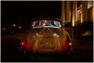 blonde bride and brunette groom in navy suit kissing in backseat of classic car with just married sign on back