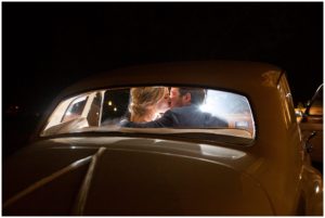 blonde bride and brunette groom in navy suit kissing in backseat of classic car after wedding