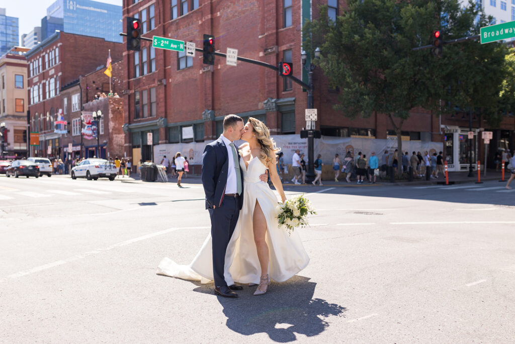 A bride and groom share a quick kiss in the middle of Broadway in Nashville on their way to their wedding at Acme Feed and Seed.