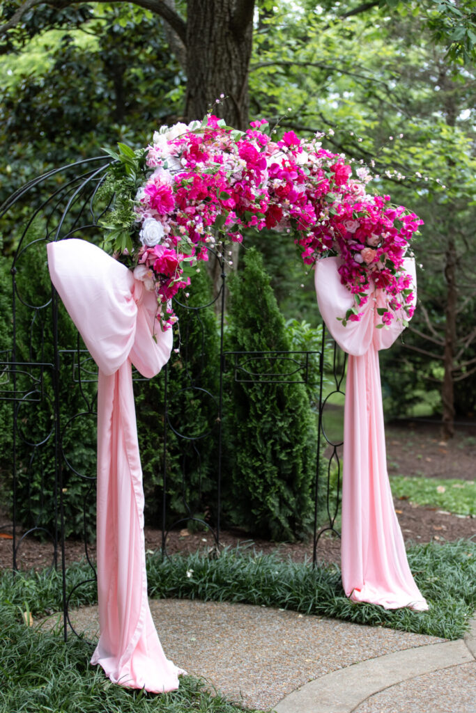 large pink wedding ceremony arch with pink flowers and large pink bows